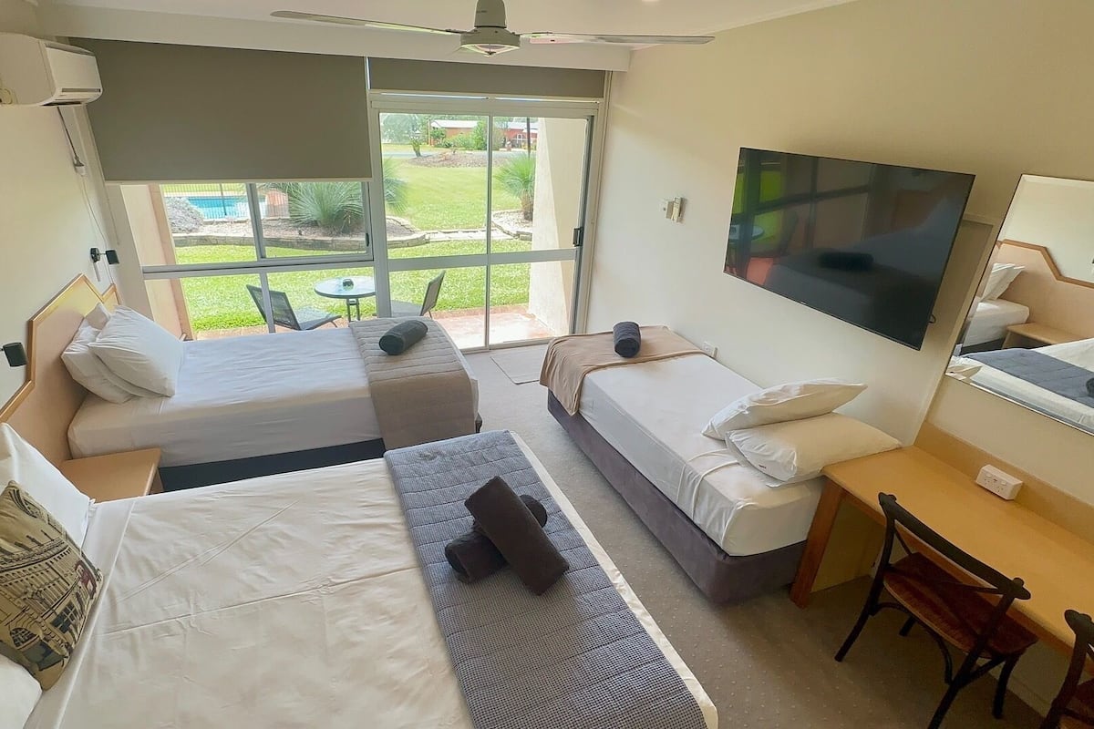 Habitación de hotel con dos camas, un escritorio, una silla, televisión y puerta corrediza de vidrio al exterior.
