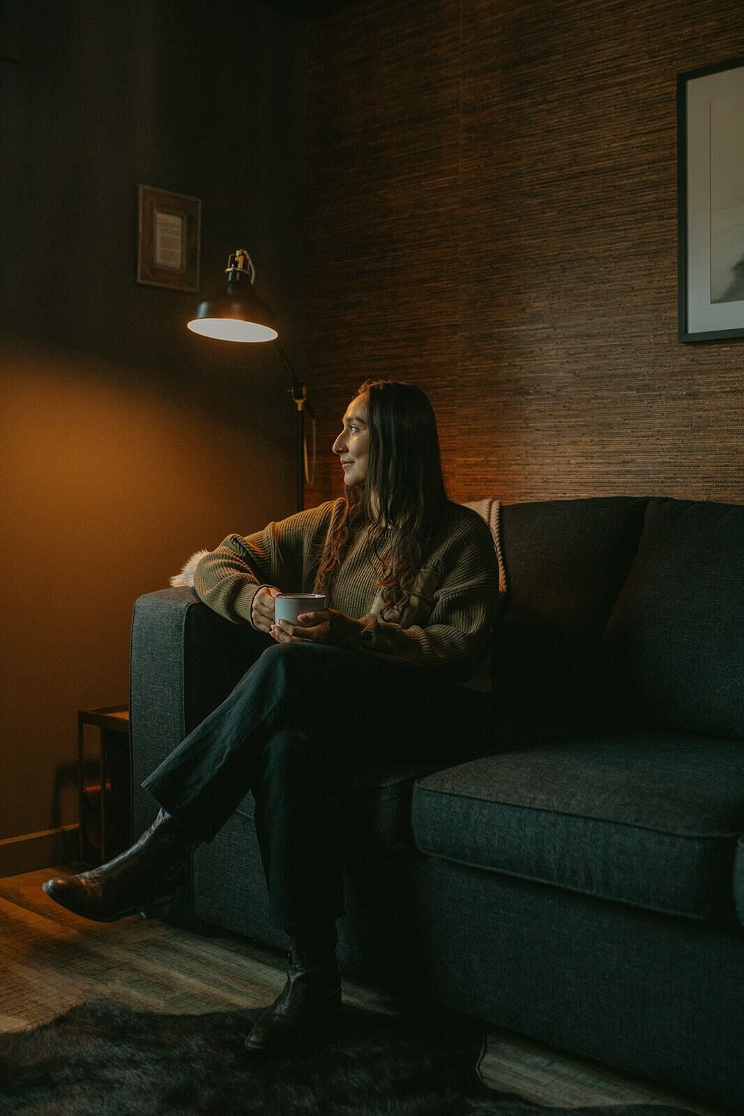 Una persona sentada en un sofá oscuro en una habitación con pared de madera y un cuadro enmarcado.