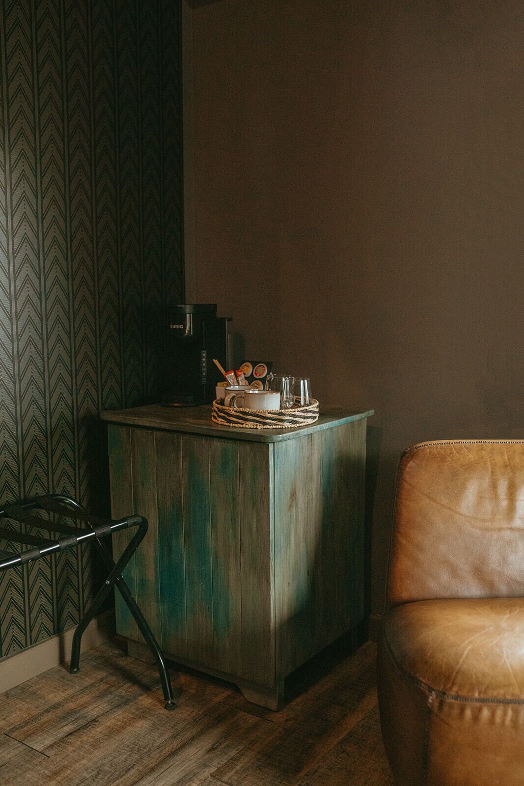 A small, rustic wooden cabinet with a woven basket on top, a coffee maker, and a glass of water.