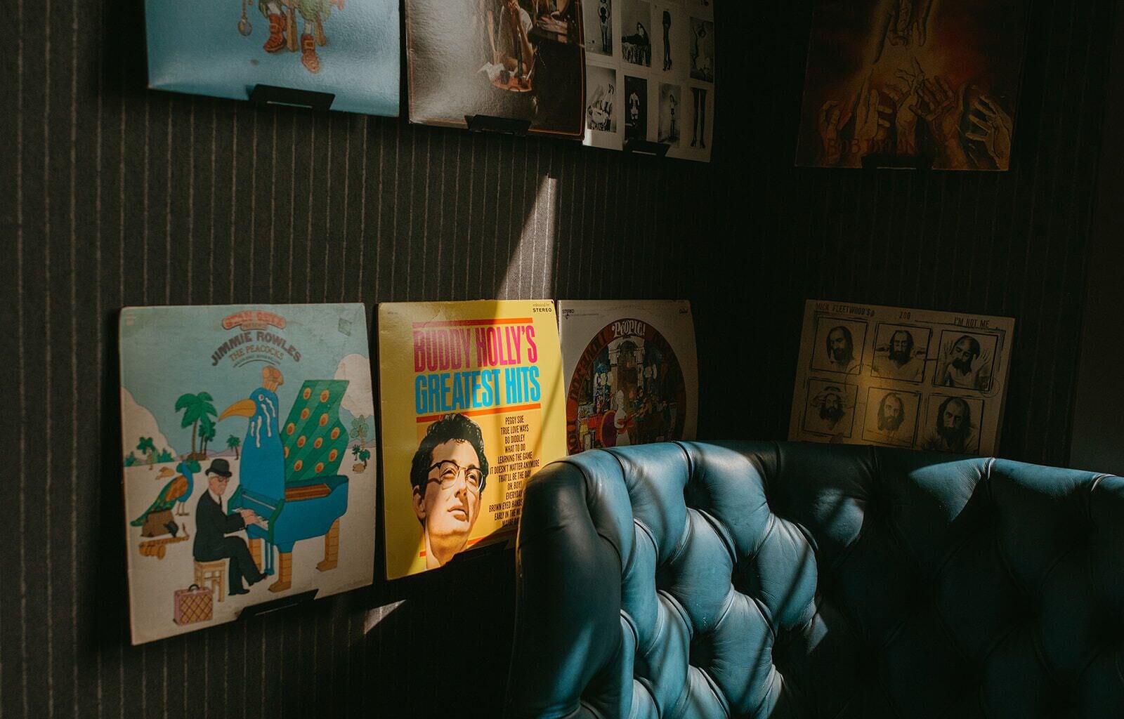 Une pièce avec un mur à rayures, un canapé en cuir bleu et divers disques vinyle exposés sur le mur.