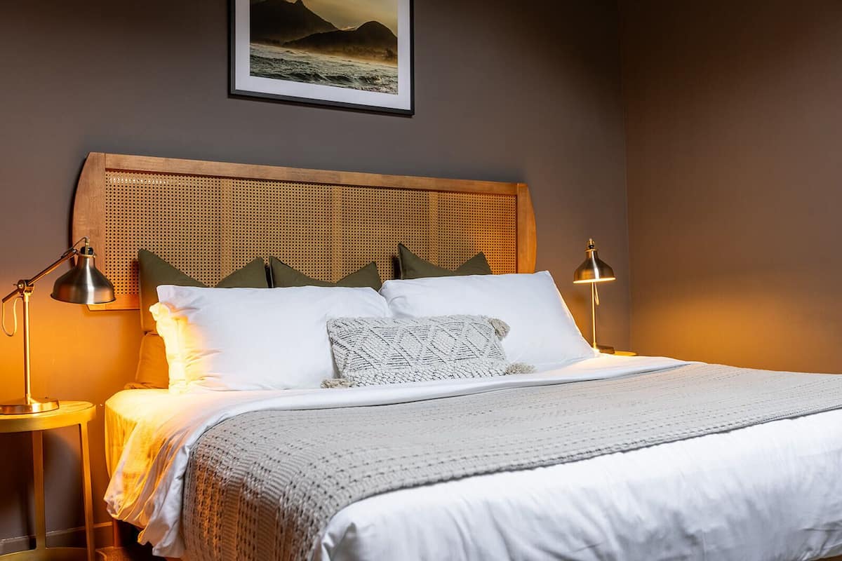 A neatly made bed with white linens and a woven headboard, flanked by two bedside lamps.