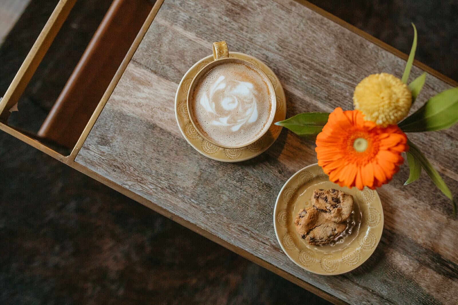 A wooden tray with a cup of coffee and a plate of cookies, accompanied by a flower.
