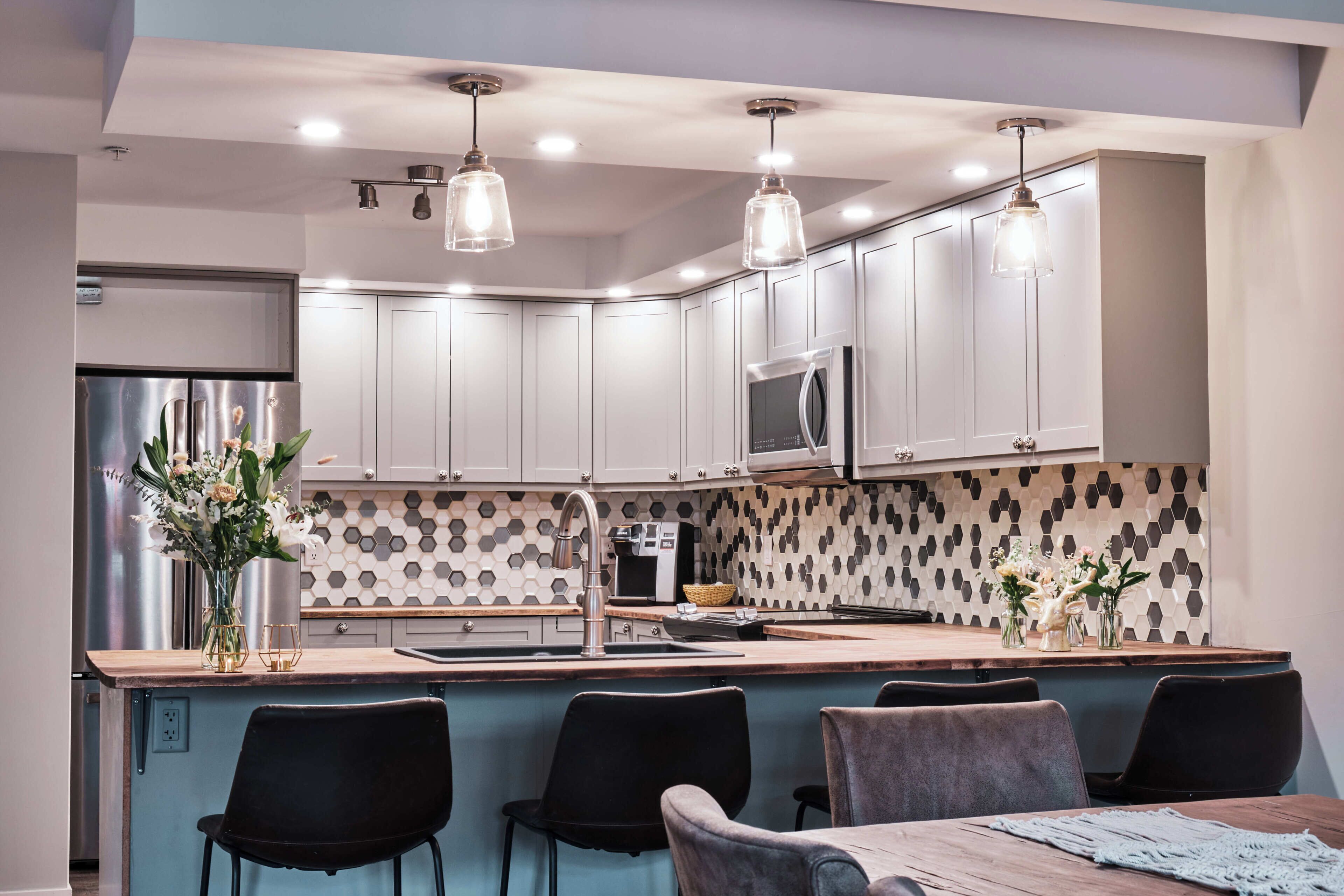 Una cocina moderna con armarios blancos, una isla central con taburetes altos, un refrigerador de acero inoxidable y un microondas.