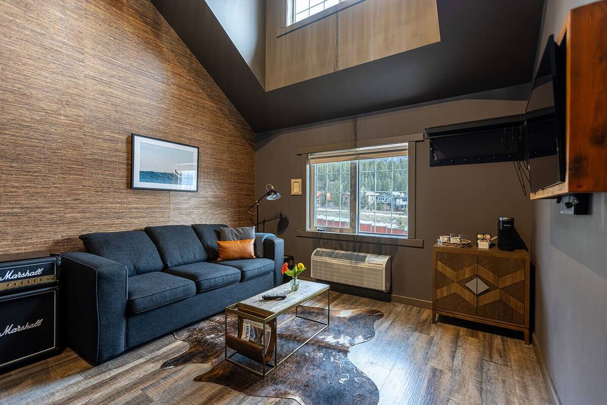 A modern living room with a dark blue sofa, a wooden accent wall, a large window, and a mounted TV.