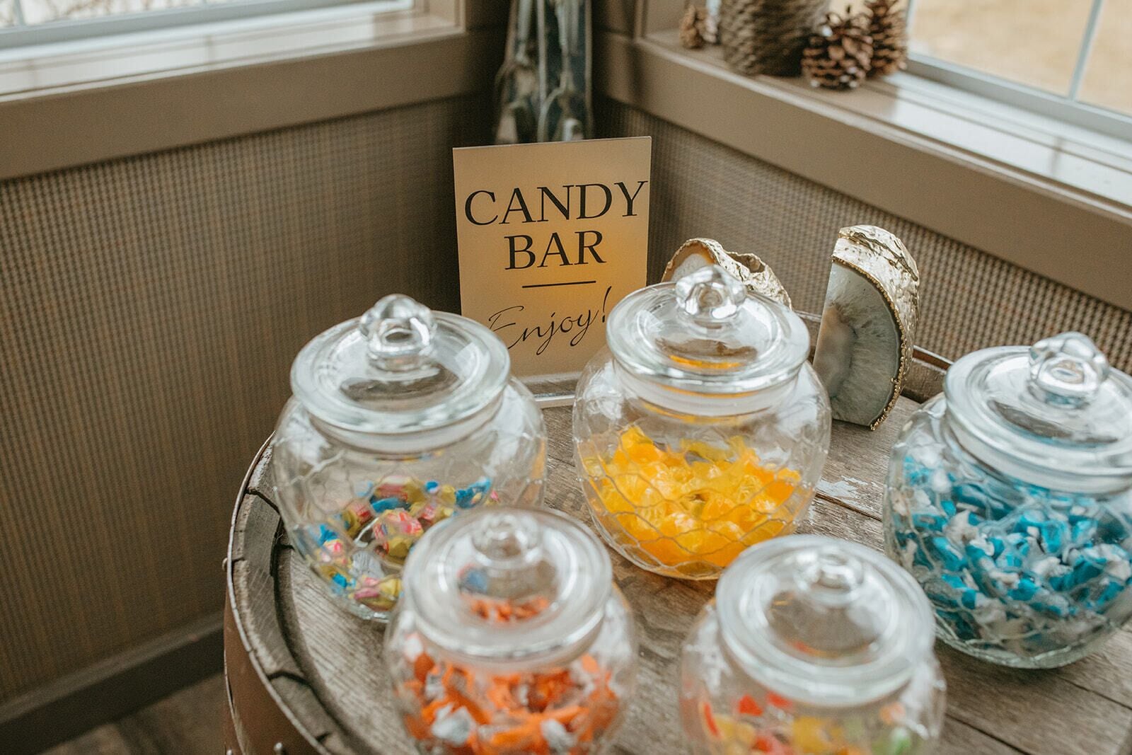 Une enseigne représentant une barre chocolatée et des bocaux remplis de bonbons colorés sont posés sur une table en bois près d’une fenêtre.