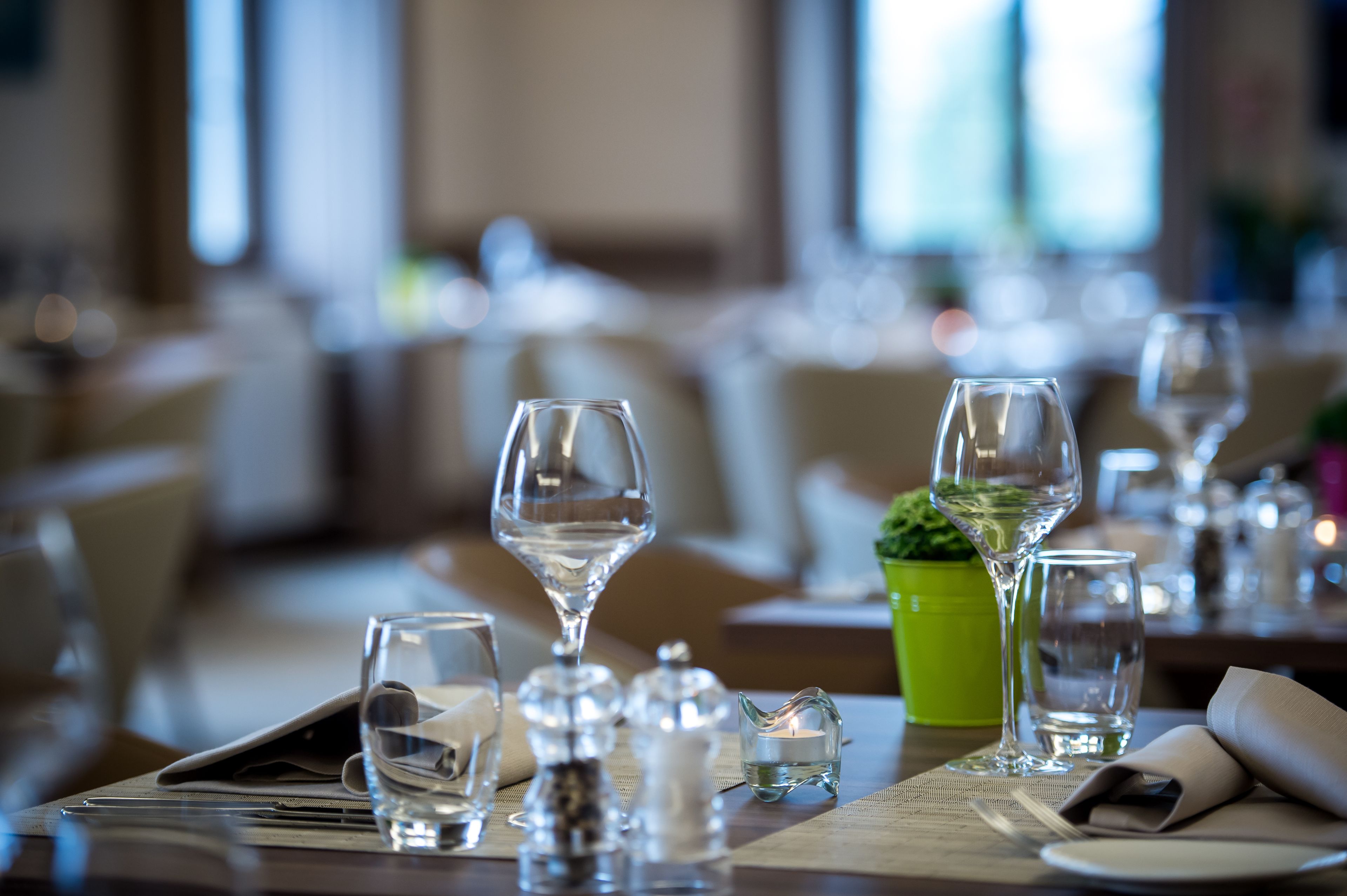 Una mesa de comedor dispuesta con varias copas de vino, una vela pequeña, saleros y pimenteros, y una planta verde.
