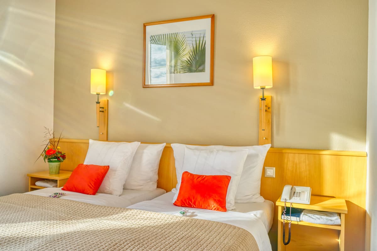 Ein Hotelzimmer mit einem Bett, zwei Nachttischen, einem Telefon und einem gerahmten Bild an der Wand.