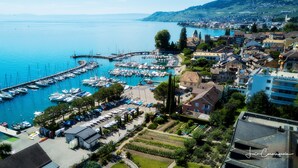 A marina with boats docked, a small building, and surrounding residential buildings. - Hôtel Bon Rivage (La Tour-de-Peilz)