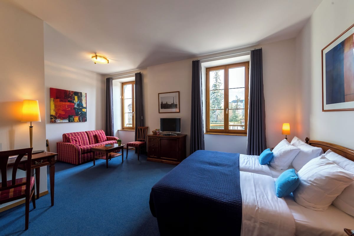 Ein Hotelzimmer mit einem großen Bett, einer Sitzecke, einem Schreibtisch und einem Fernseher.