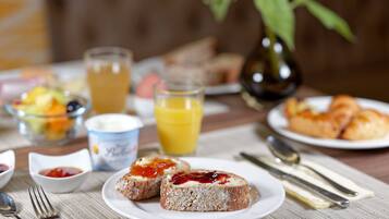 Ein Frühstückstisch mit Toast, Marmelade, Butter, einem Glas Orangensaft, einer Obstschale und einer Vase mit einer Sonnenblume.