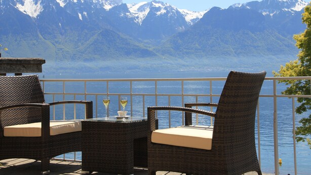 A terrace with wicker furniture and a table, overlooking a lake and mountains. - Hôtel Bon Rivage (La Tour-de-Peilz)