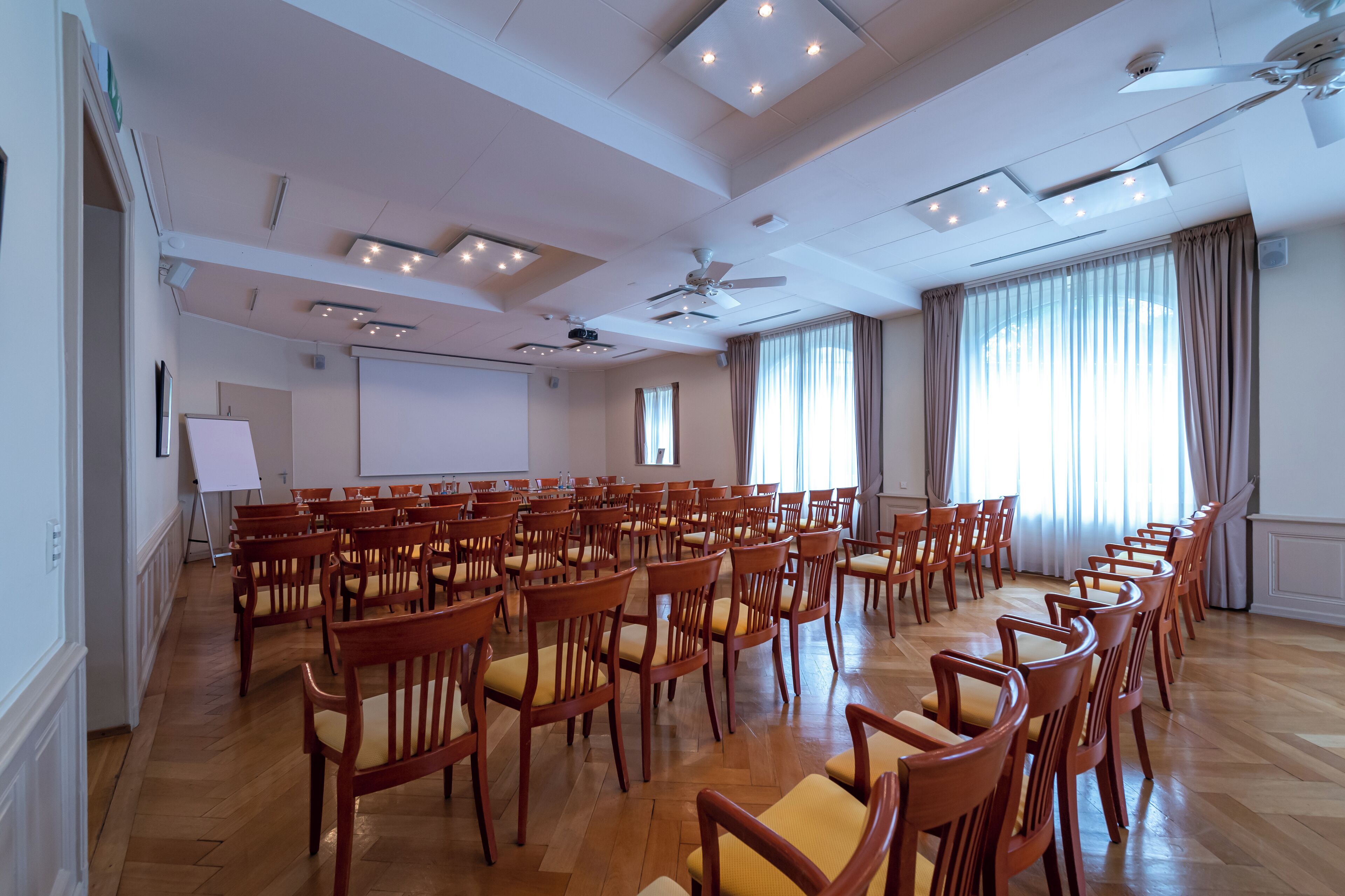 Un salón de conferencias con filas de sillas de madera, una pizarra y una pantalla para proyector.