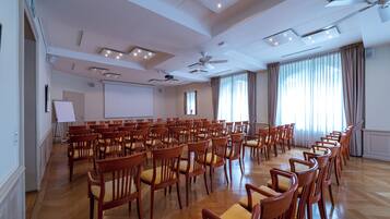 Un salón de conferencias con filas de sillas de madera, una pizarra y una pantalla para proyector.