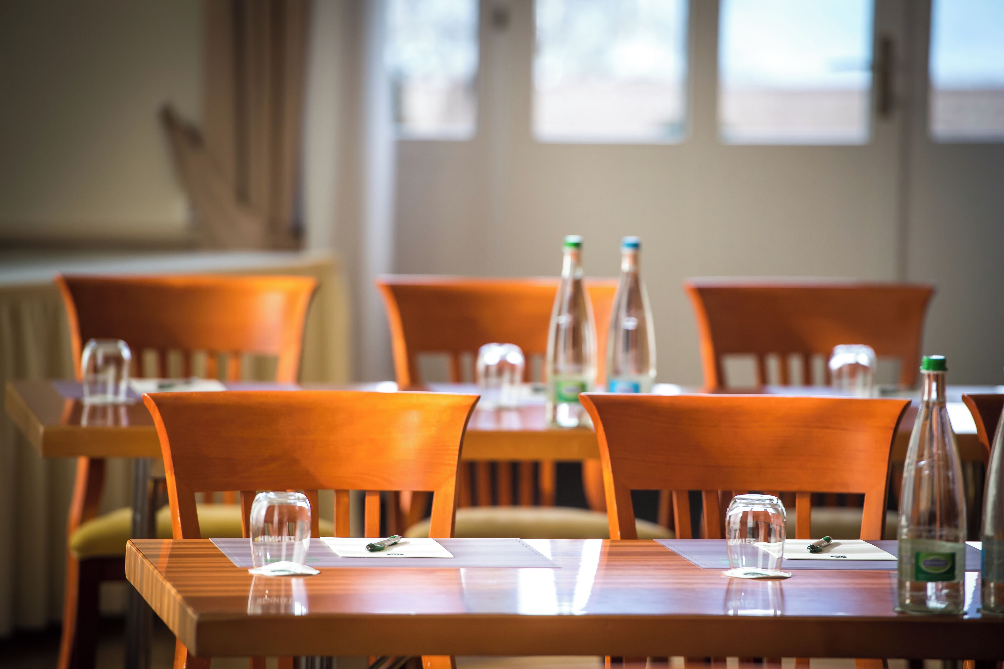 Un comedor con mesas y sillas de madera, vasos transparentes y botellas de agua.