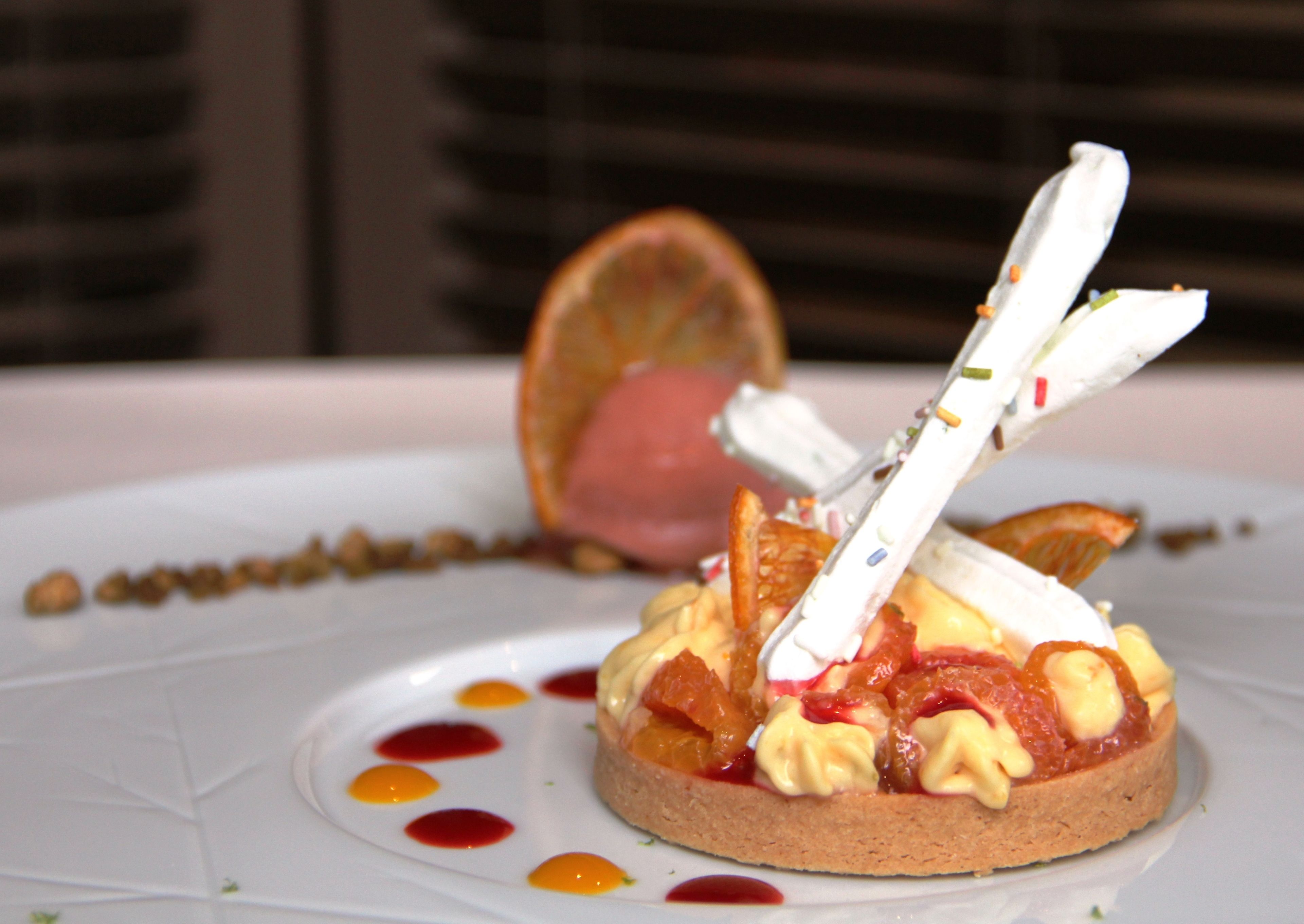 Een dessert op een wit bord, met een sinaasappelschijfje en een vork.