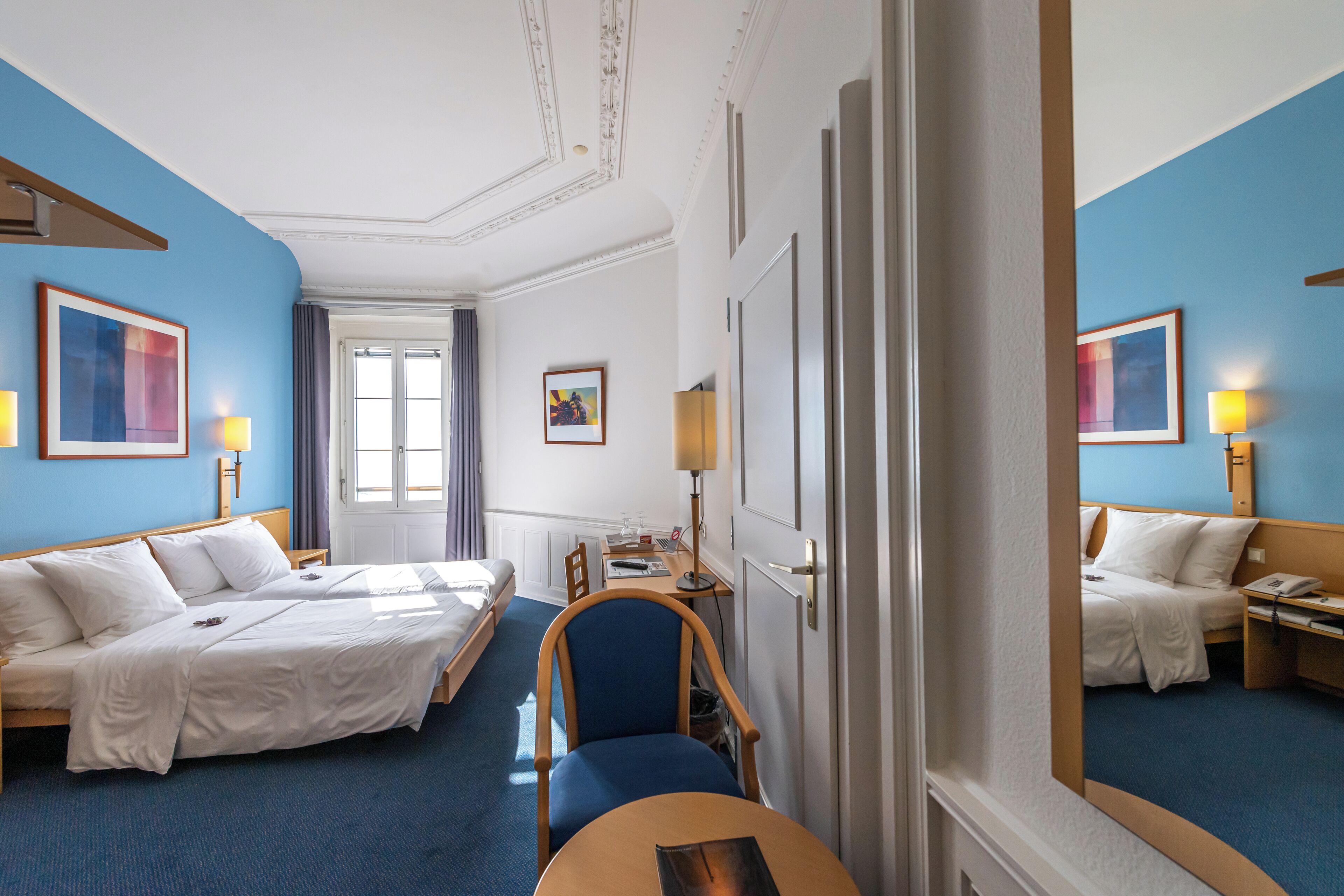Une chambre d’hôtel avec deux lits, un bureau, une chaise et un miroir.