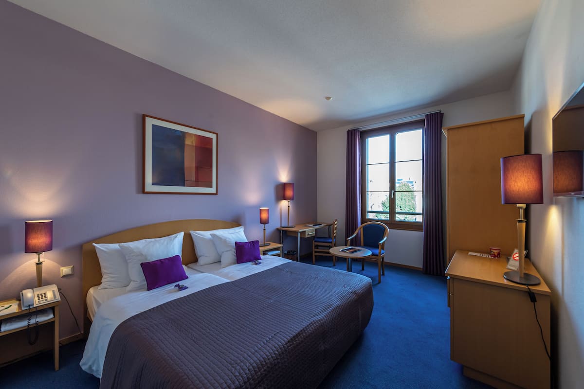 Ein Hotelzimmer mit einem großen Bett, einem Schreibtisch, einem Stuhl und einem kleinen Tisch.