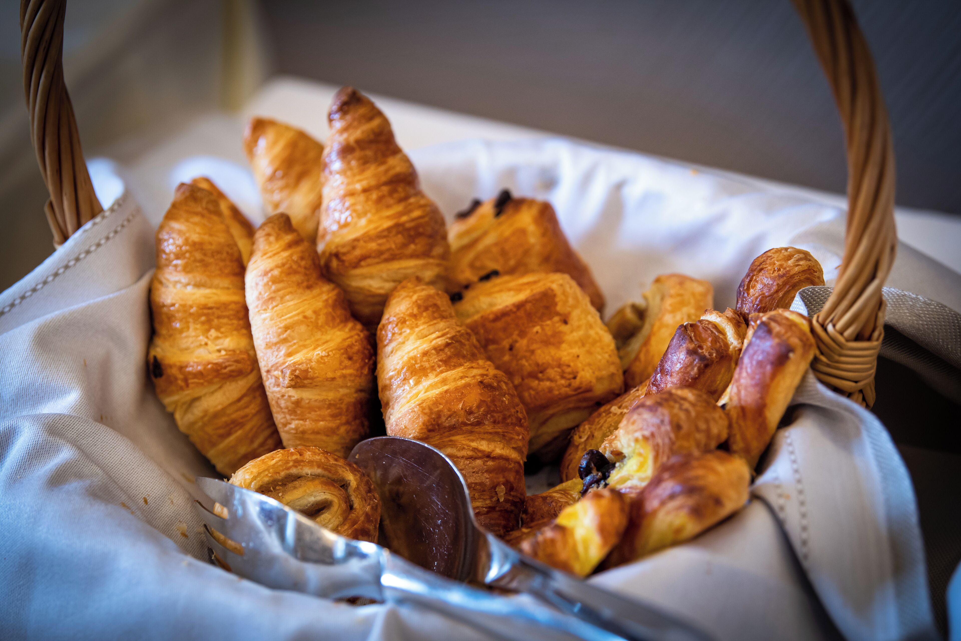 A basket of assorted pastries, including croissants and a chocolate éclair, placed on a white cloth.