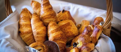 A basket of assorted pastries, including croissants and a chocolate éclair, placed on a white cloth.