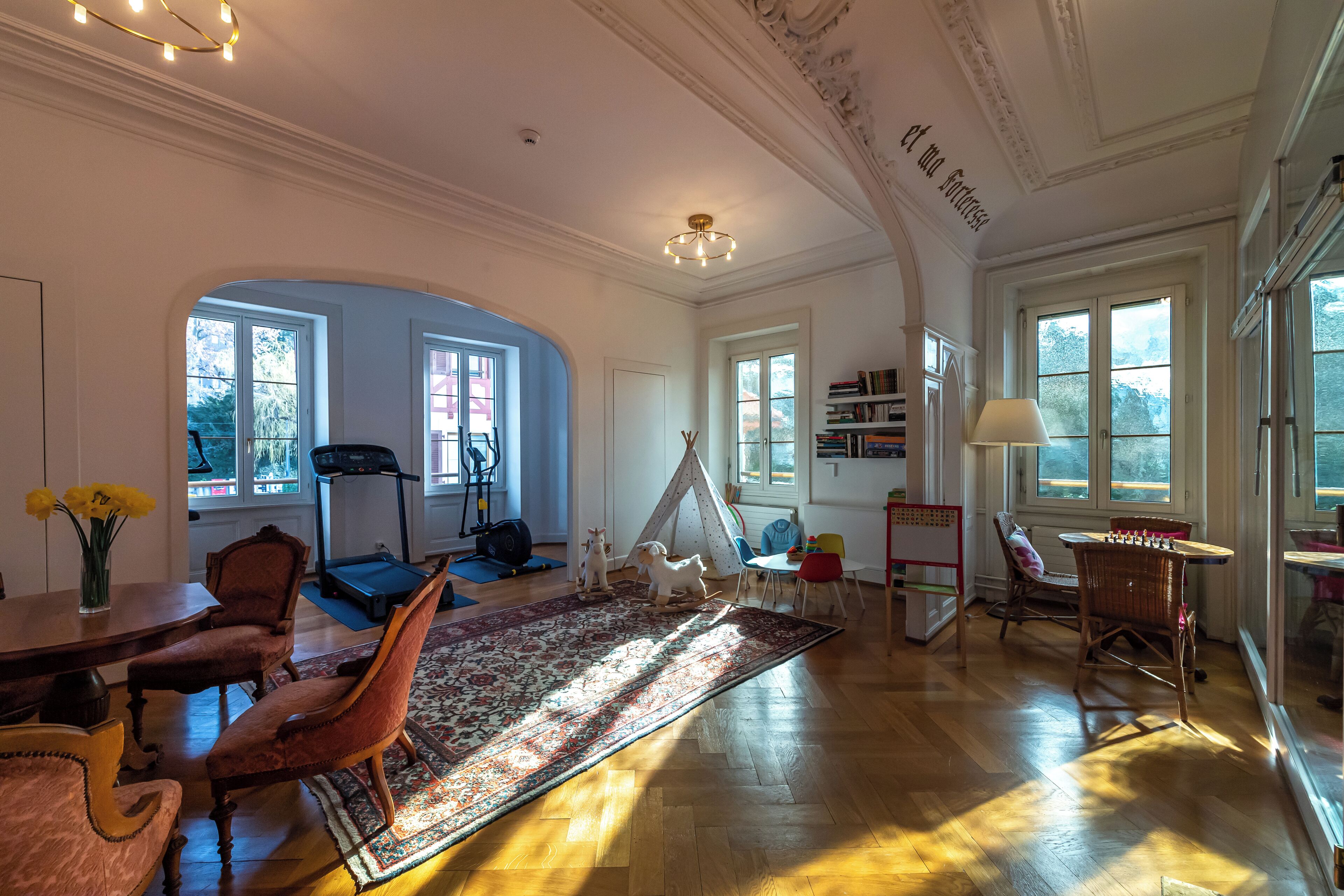 A spacious living room with a large rug, wooden flooring, and a tent set up in the center.