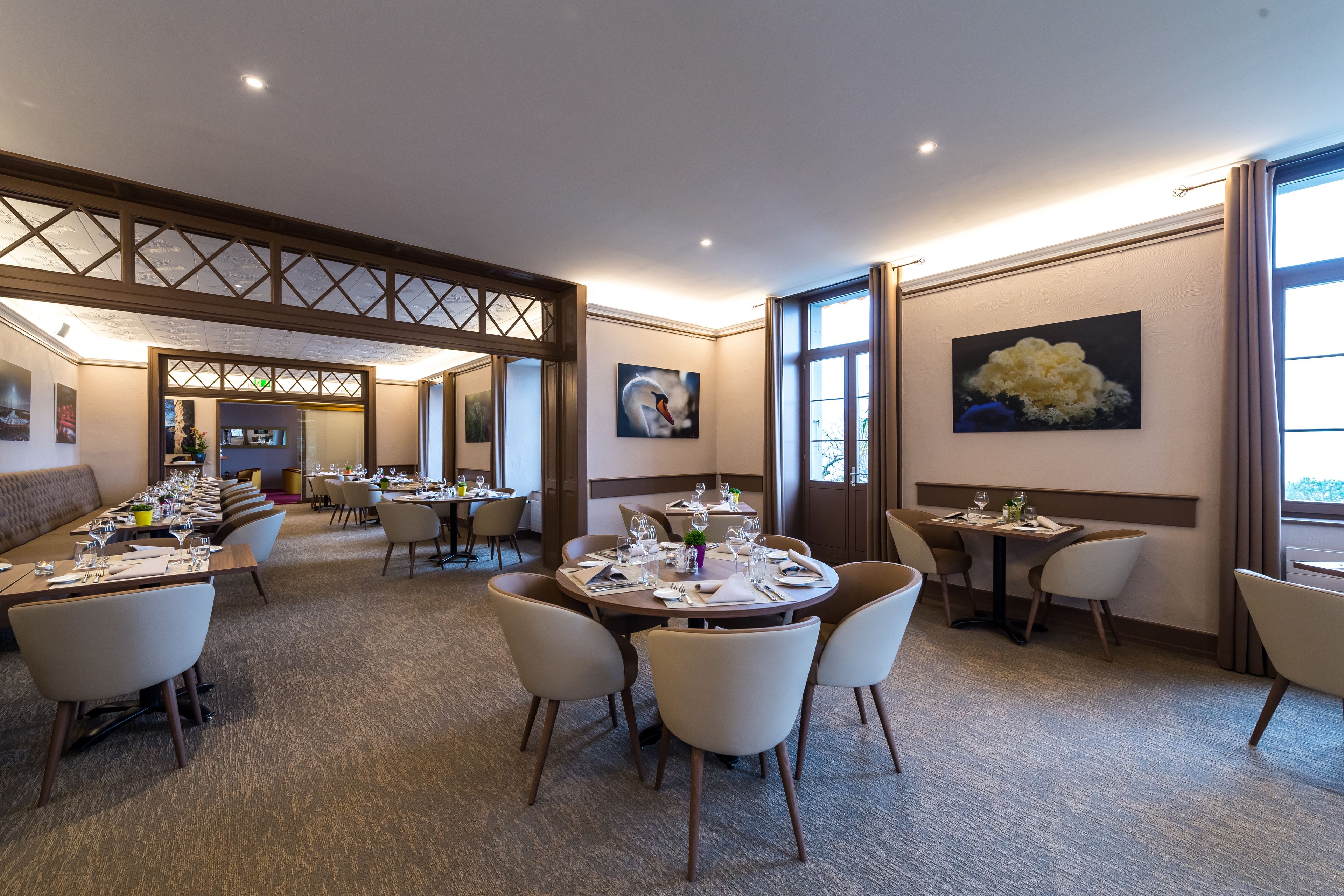 A hotel dining area with multiple round tables, chairs, and a long communal table.