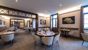 A hotel dining area with multiple round tables, chairs, and a long communal table.