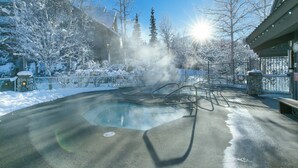 A heated outdoor pool surrounded by snow-covered trees and a building with a stone facade. - The Aspens by Whistler Premier (Whistler)