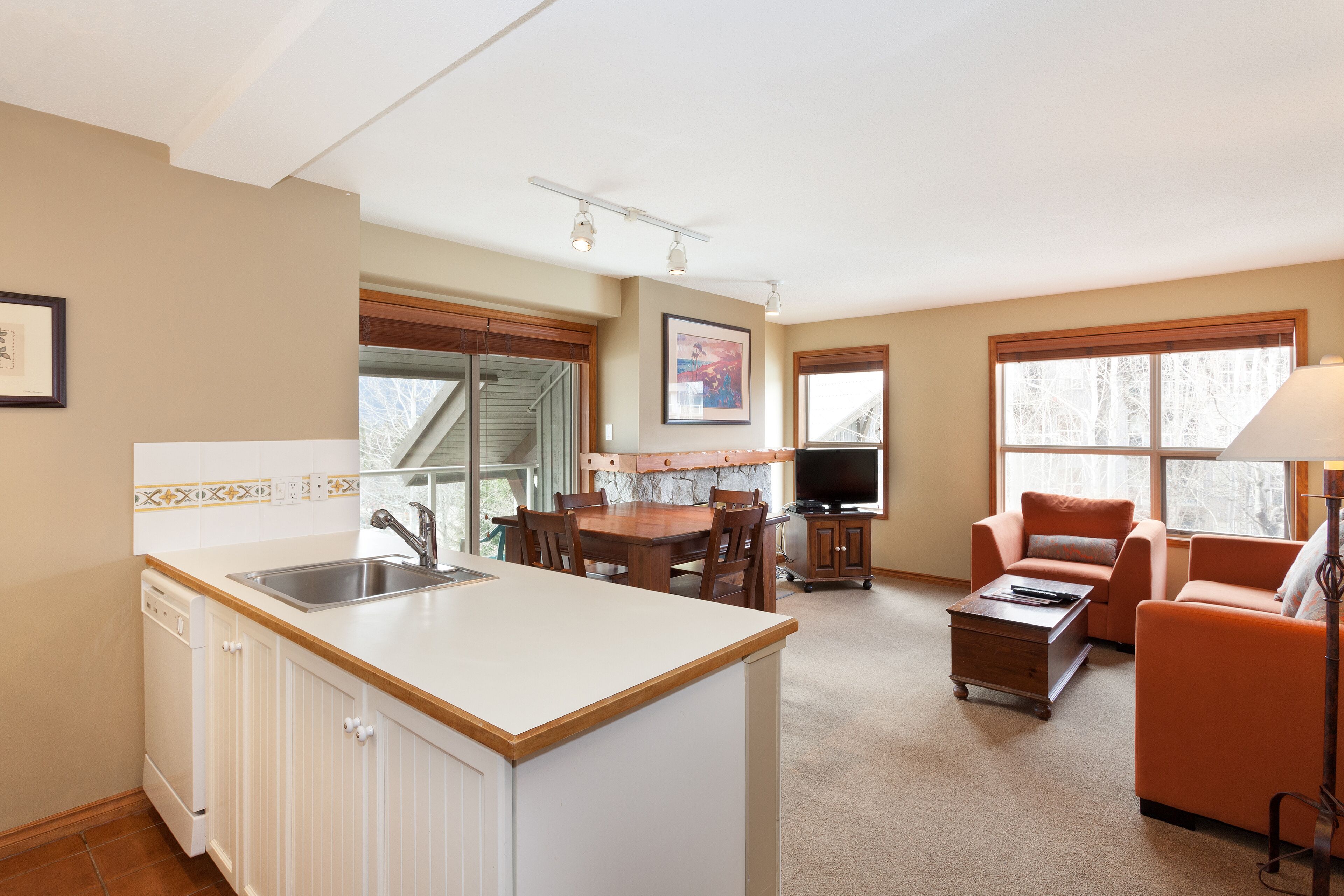 A kitchen with a central island, dining table, and chairs, a living area with a sofa and armchair, and a television.