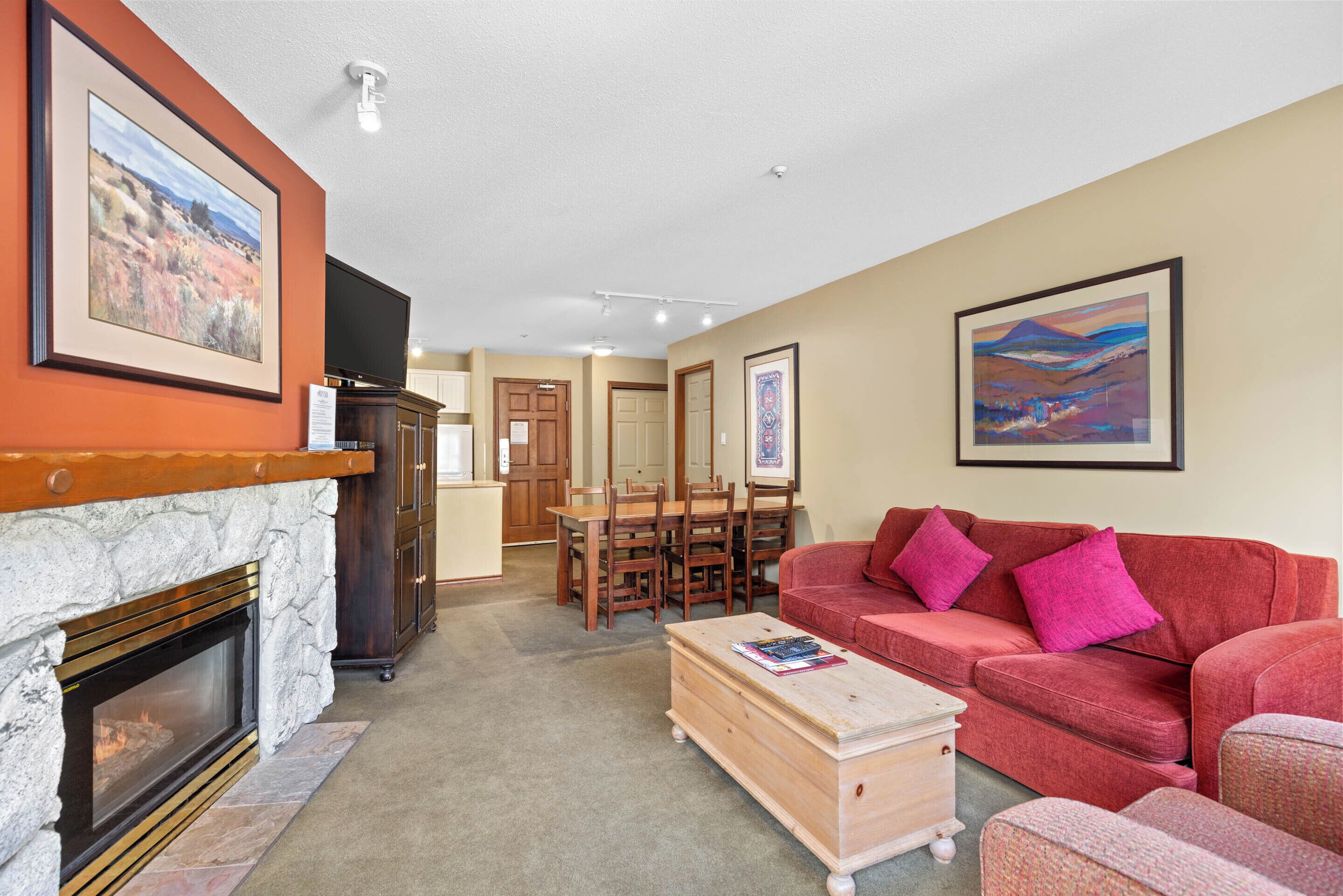 A living room with a fireplace, a red sofa, a wooden coffee table, and a dining area with a table and chairs.
