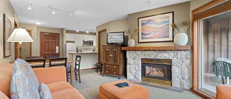 A living room with a fireplace, orange sofas, and a dining area in the background.