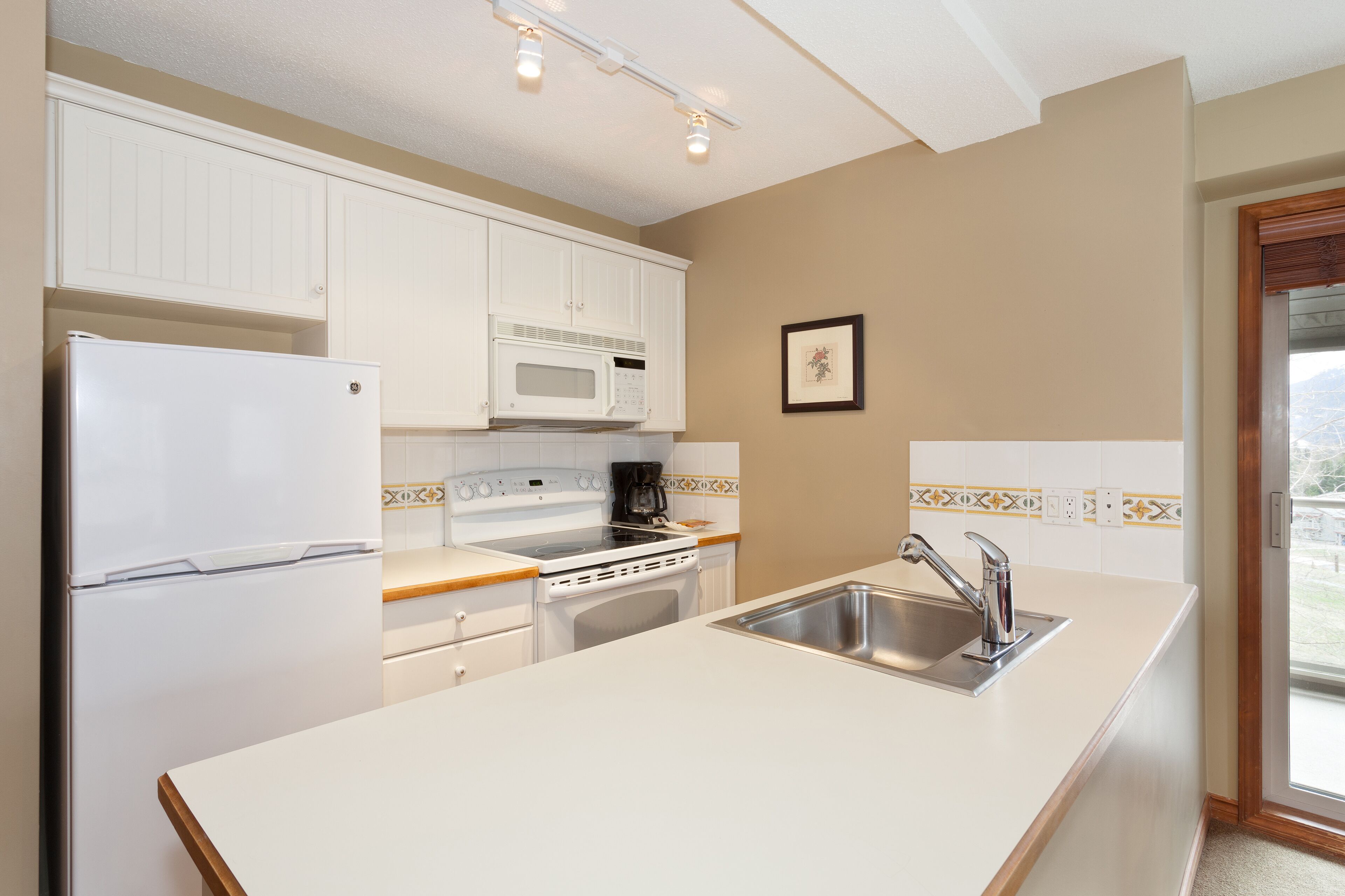 Una cocina con armarios blancos, microondas, estufa y lavabo.