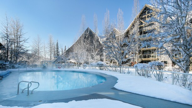 A snow-covered outdoor pool area with a clear sky, surrounded by buildings and trees. - The Aspens by Whistler Premier (Whistler)