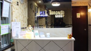Un comptoir d’accueil avec une horloge, une enseigne indiquant « Toronto Motel Group », et une petite figurine.
