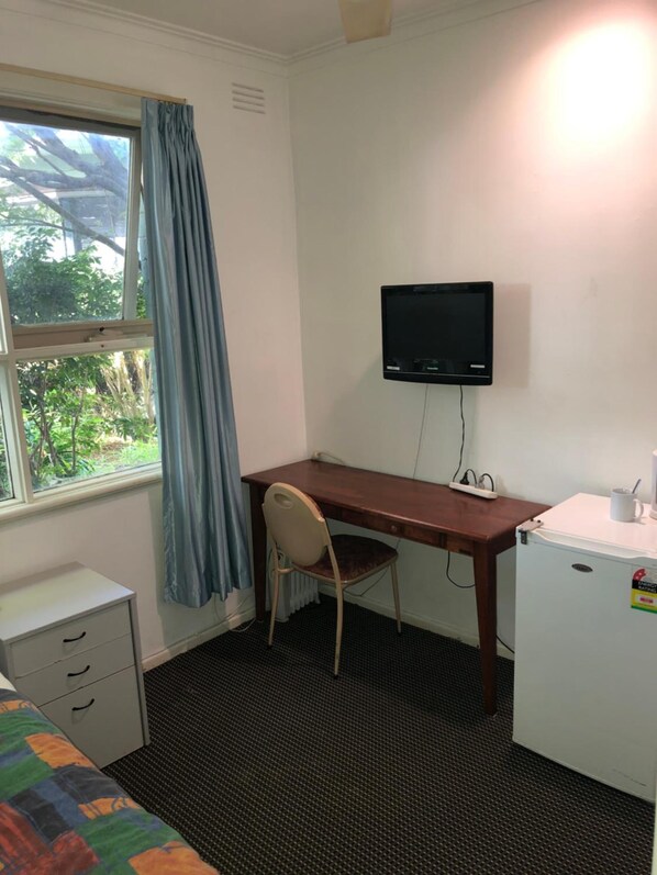 Una habitación pequeña con cama, escritorio, silla, televisor y refrigerador.