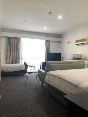 A hotel room with two beds, a desk, a chair, a television, and an air conditioning unit. - Evancourt Motel (Malvern East)