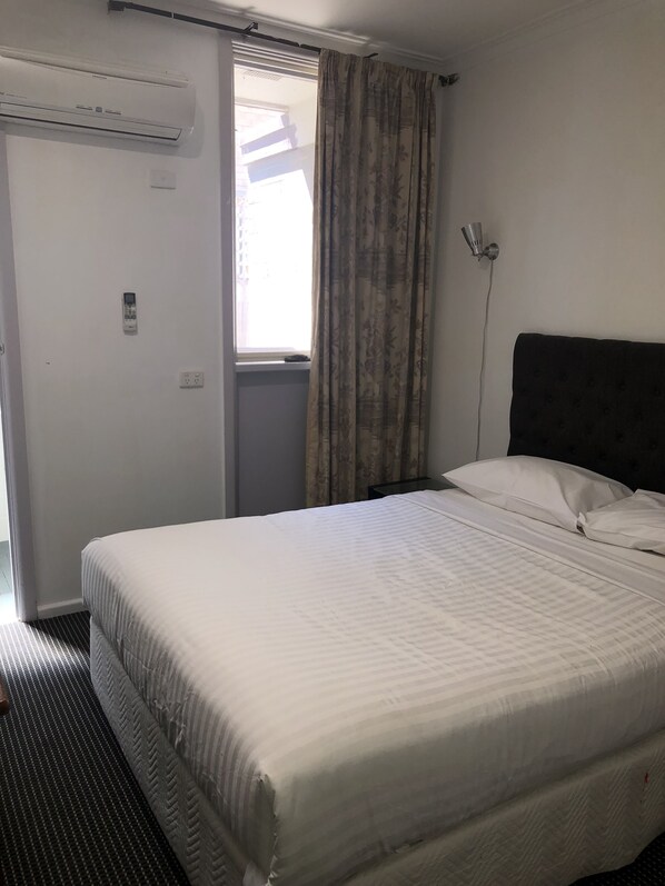 A hotel room with a bed, a window with curtains, an air conditioning unit, and a wall-mounted phone. - Evancourt Motel (Malvern East)