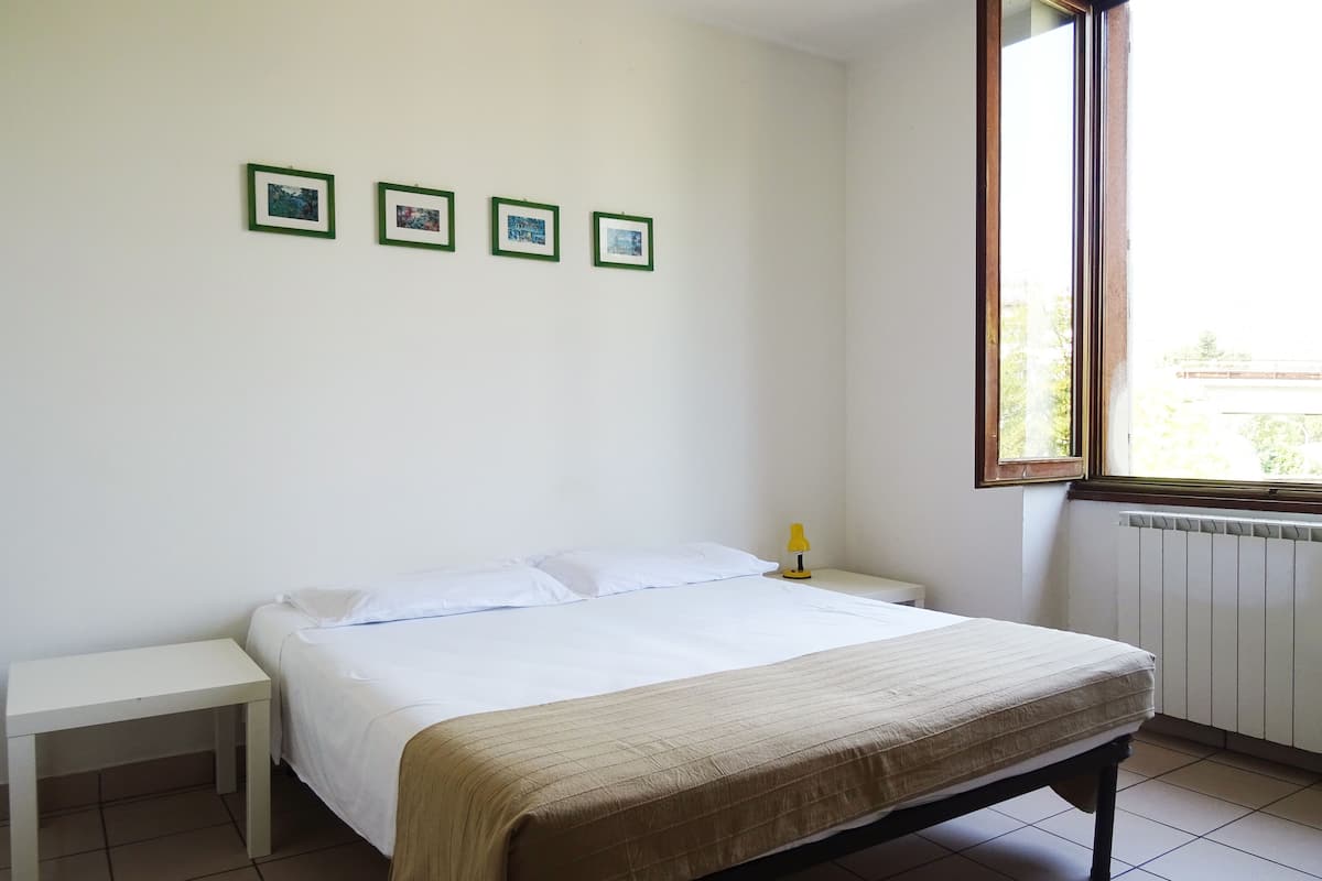 A bedroom with a bed, a bedside table, a window, and three framed pictures on the wall.