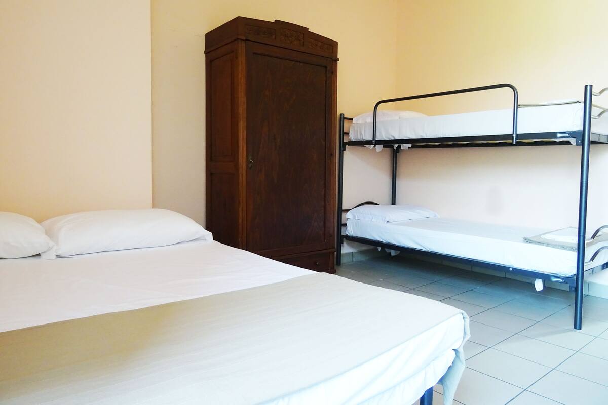 A single bed with a wooden wardrobe and a bunk bed in a room with white walls and tiled floor.