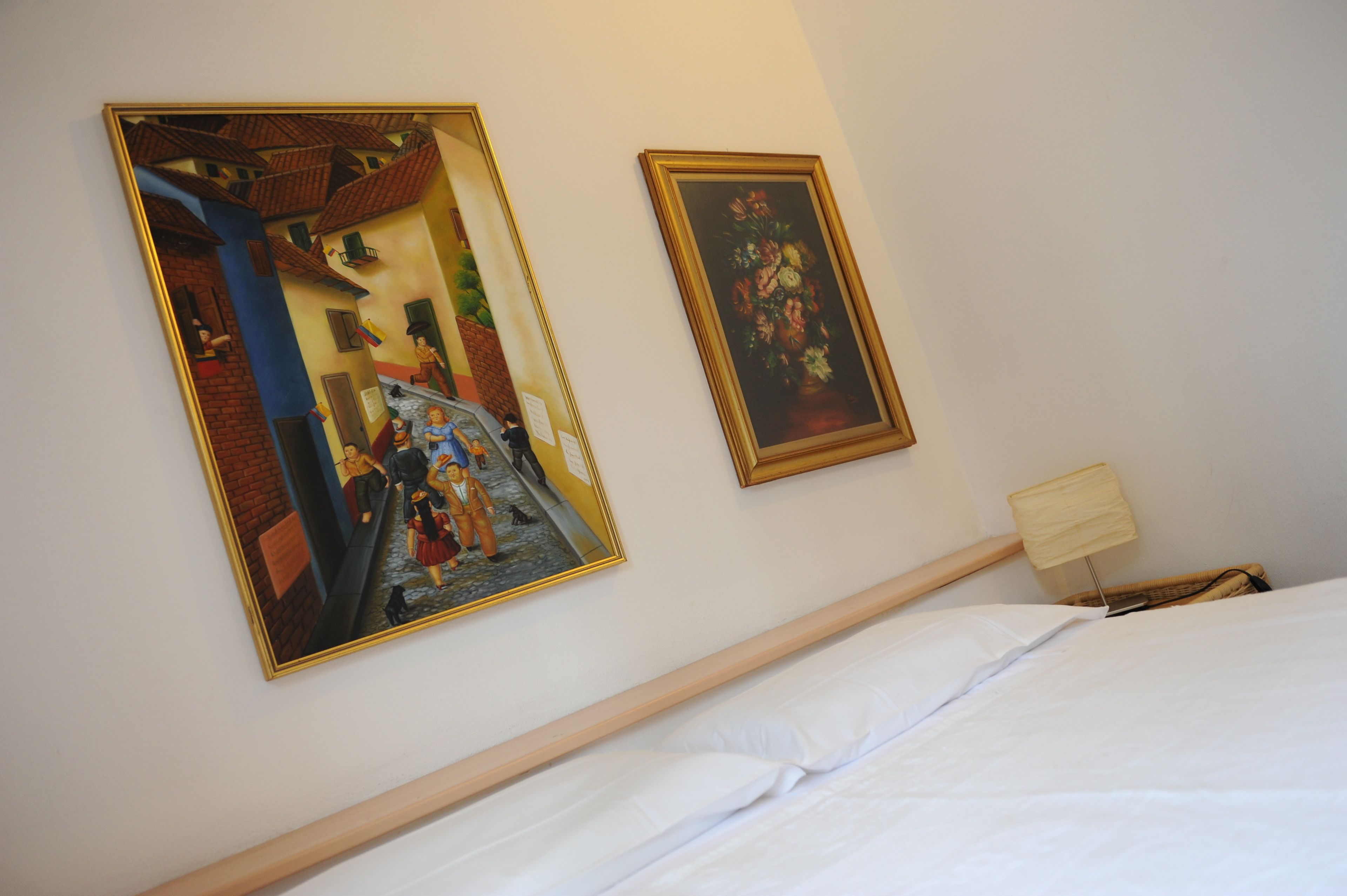 A hotel room with a bed, a nightstand, a lamp, and two framed artworks on the wall.