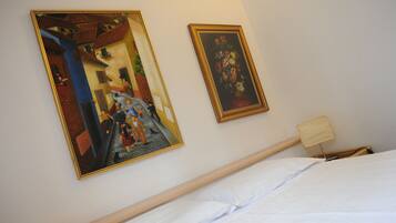 A hotel room with a bed, a nightstand, a lamp, and two framed artworks on the wall.