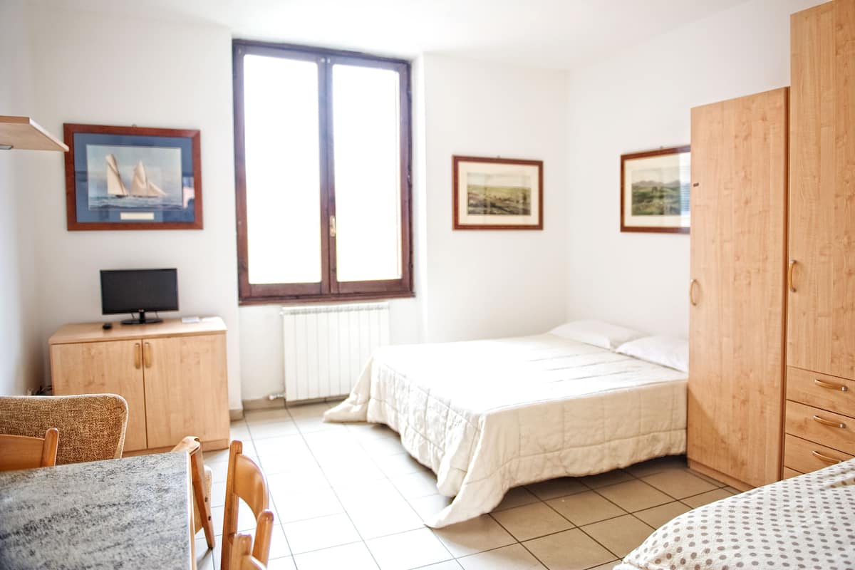 A bedroom with a bed, a wooden wardrobe, a television on a cabinet, and two framed pictures on the wall.