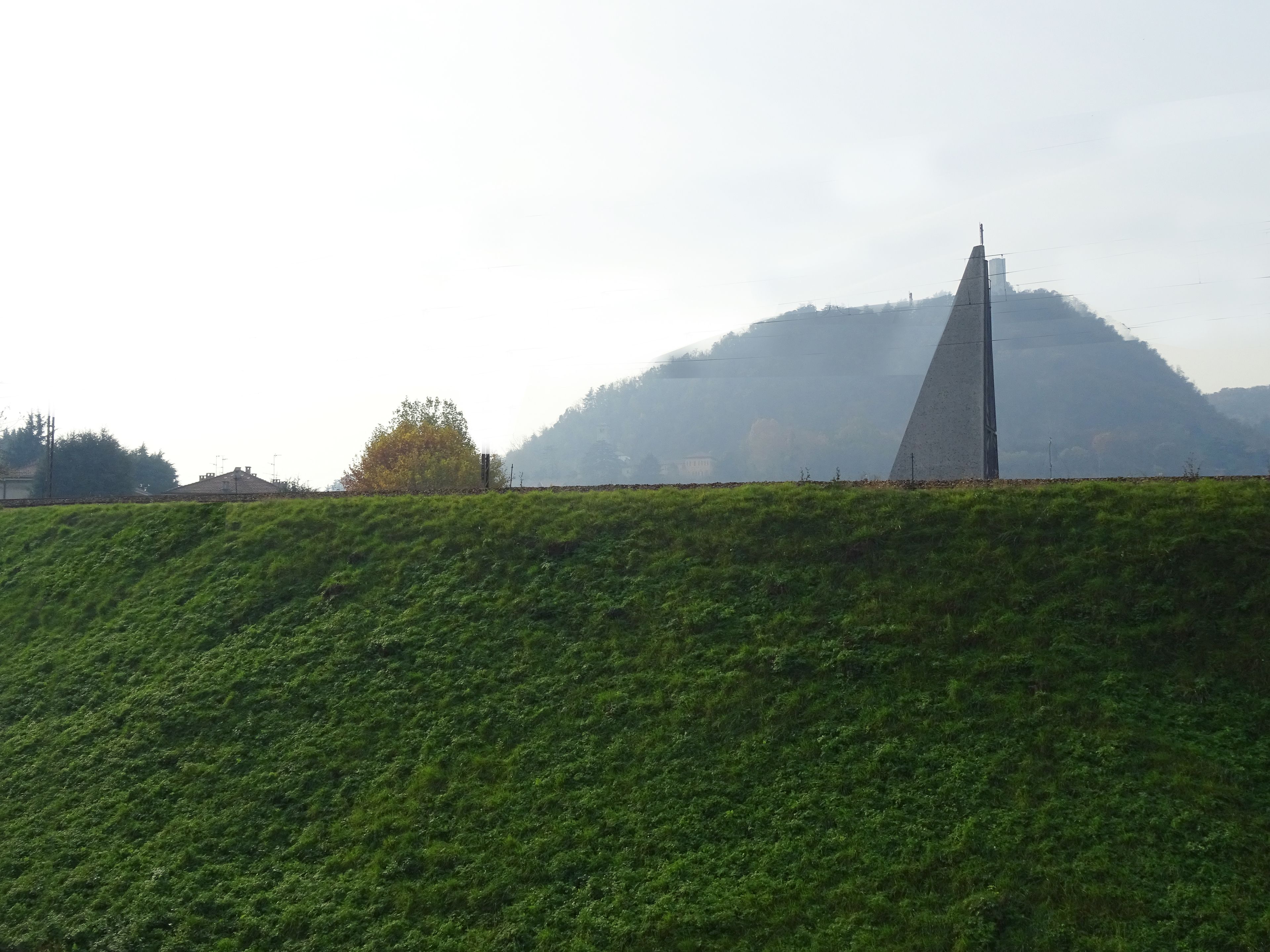 A grassy hill with a monument and a mountain in the background.