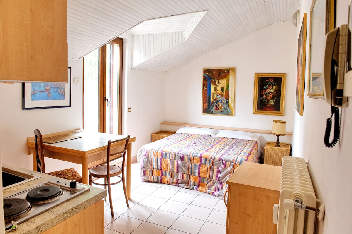 A compact room with a bed, a desk, and a chair. There is a window providing natural light.