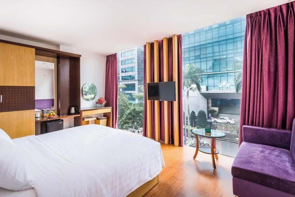 A hotel room with a bed, a desk, a TV, and a view of a cityscape.