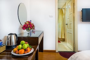 A hotel room with a wooden desk, a plate of fruit, a vase of flowers, a mirror, a coffee maker, and a television. - Tu Sakura Hotel (Hanoi)