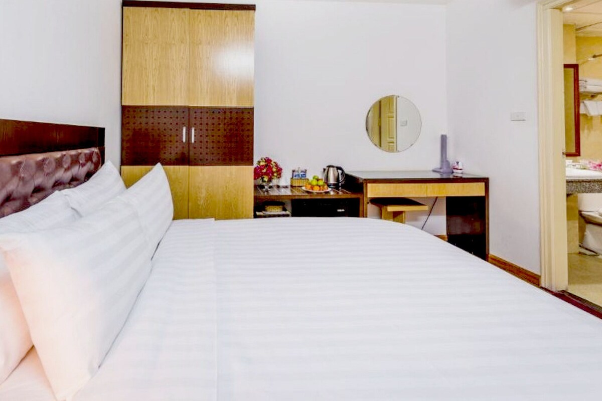 A hotel room with a bed, a desk, a mirror, and a bathroom visible through an open door.