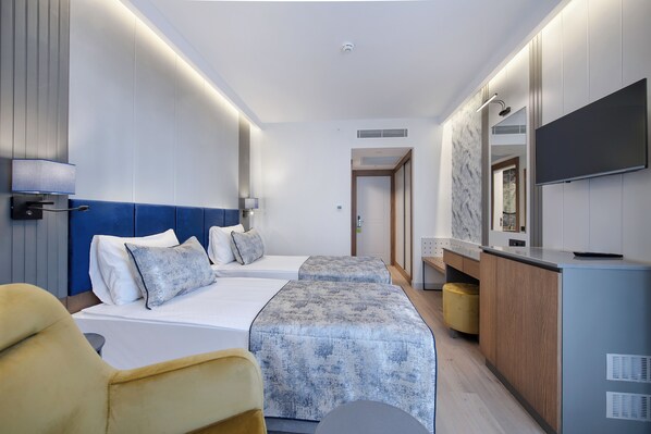 Una habitación de hotel moderna con dos camas, un escritorio, una televisión y un baño visible a través de una puerta abierta.
