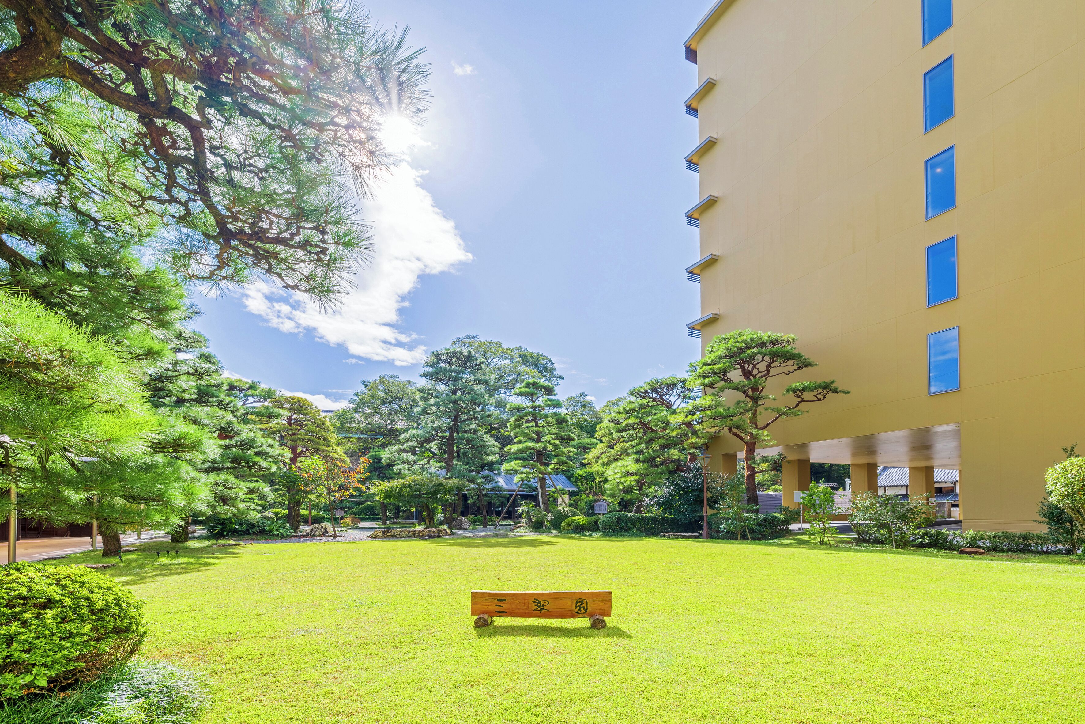 A courtyard with a bench, surrounded by trees and a building with blue windows.