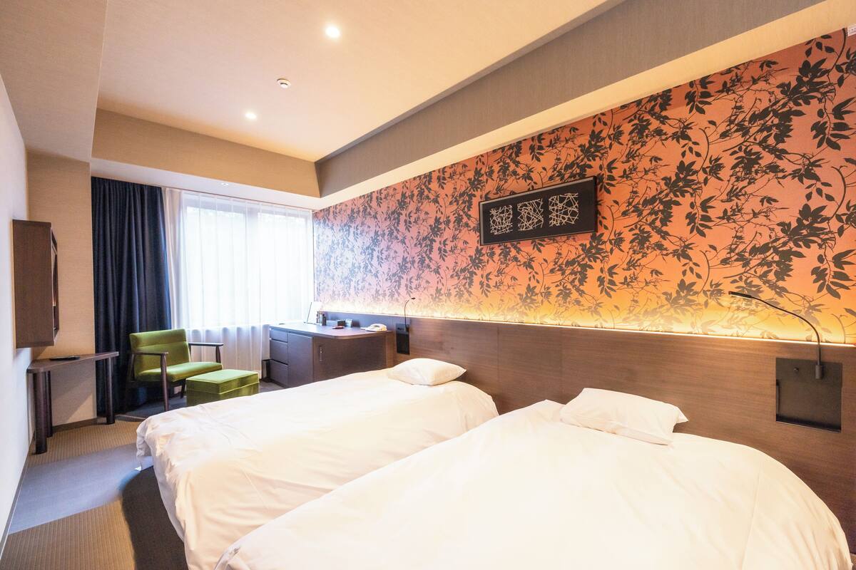 Habitación de hotel con dos camas, un escritorio, una silla y un detalle decorativo en la pared.