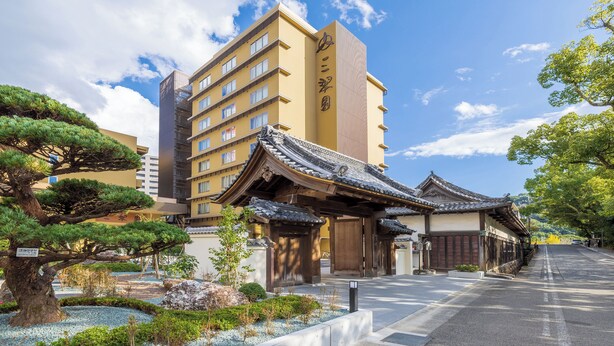 A traditional Japanese building with a modern high-rise in the background. - Sansuien (Kochi)